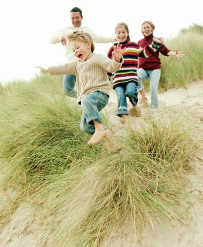 Happy family jumping through sand dunes at the beach.