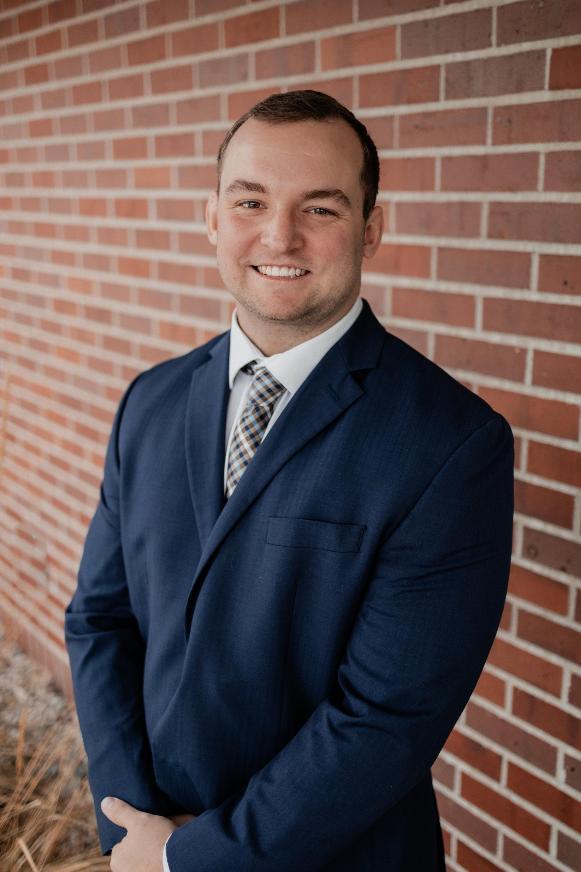 Bret Klabunde smiling in a suit against a brick wall.