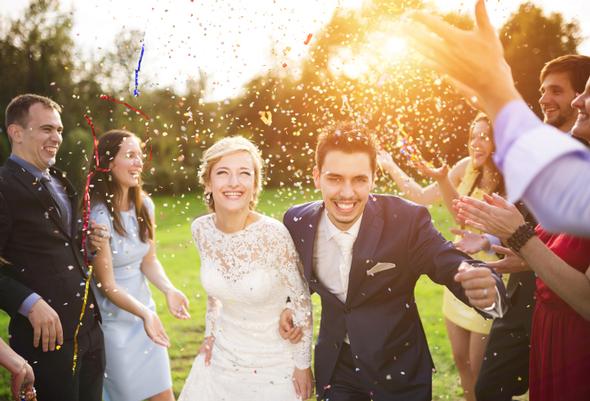 Newlyweds celebrating under falling confetti with friends.