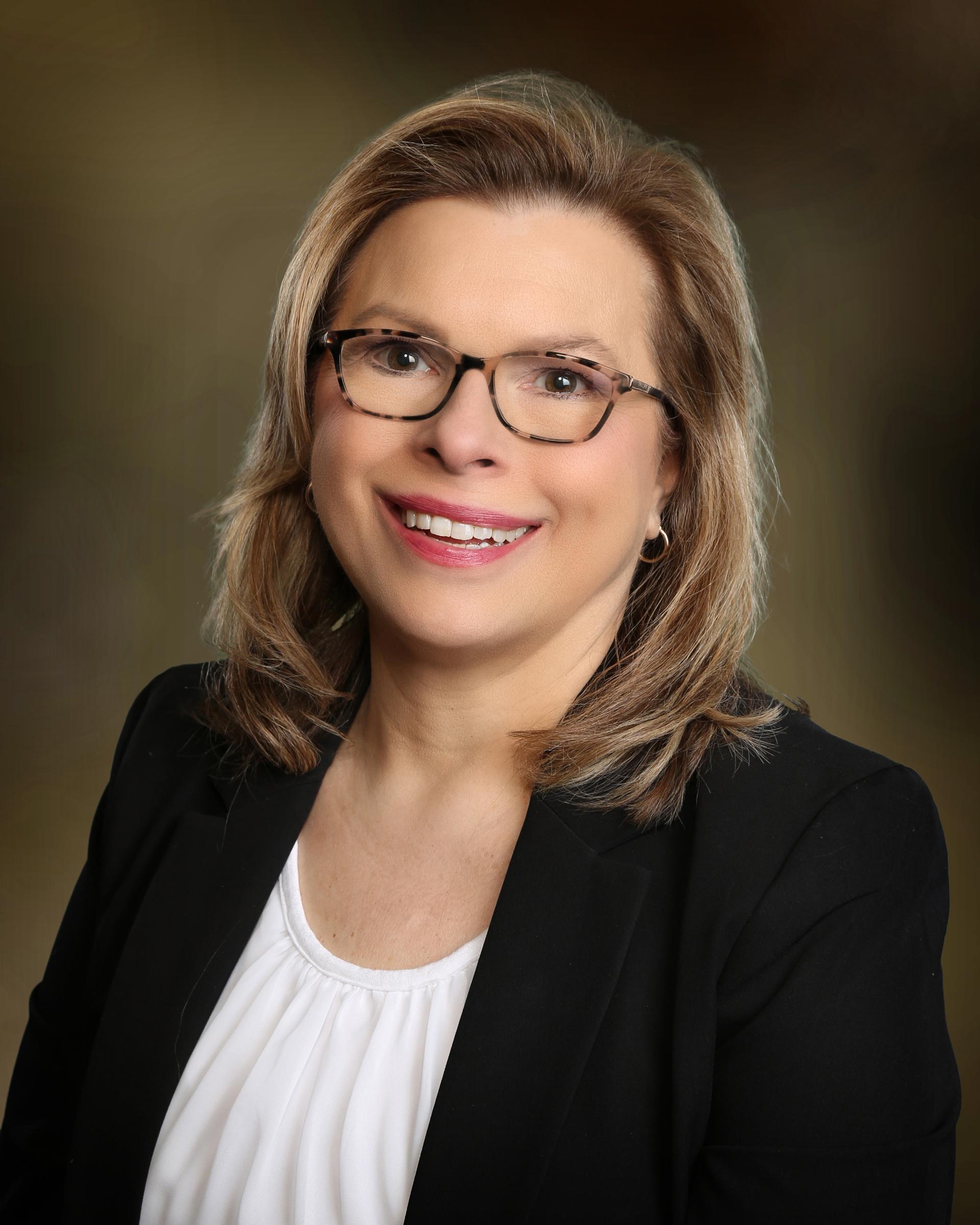 Smiling blonde team member wearing glasses and a black blazer.