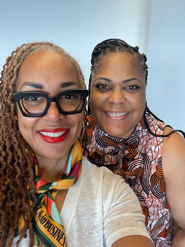 Two smiling women with braided hair posing for a photo.