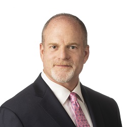 Adam Miller wearing a dark suit and pink patterned tie