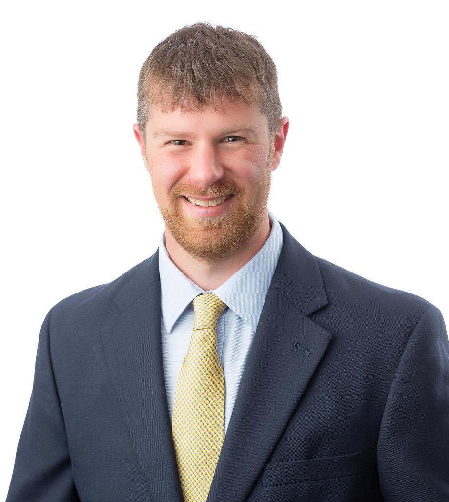 Smiling man with a beard in a blue suit and gold tie.