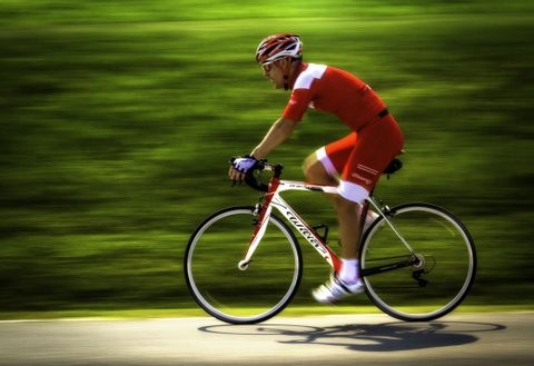 Cyclist in red gear riding a road bike past green fields