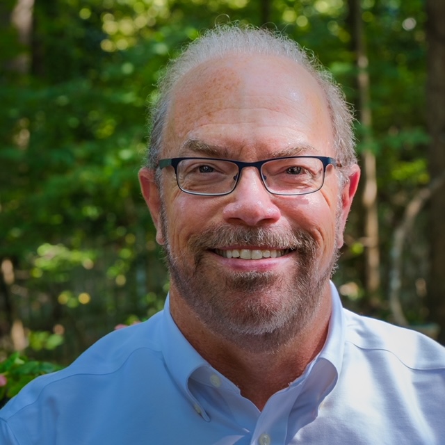 A person with glasses smilingDescription automatically generated