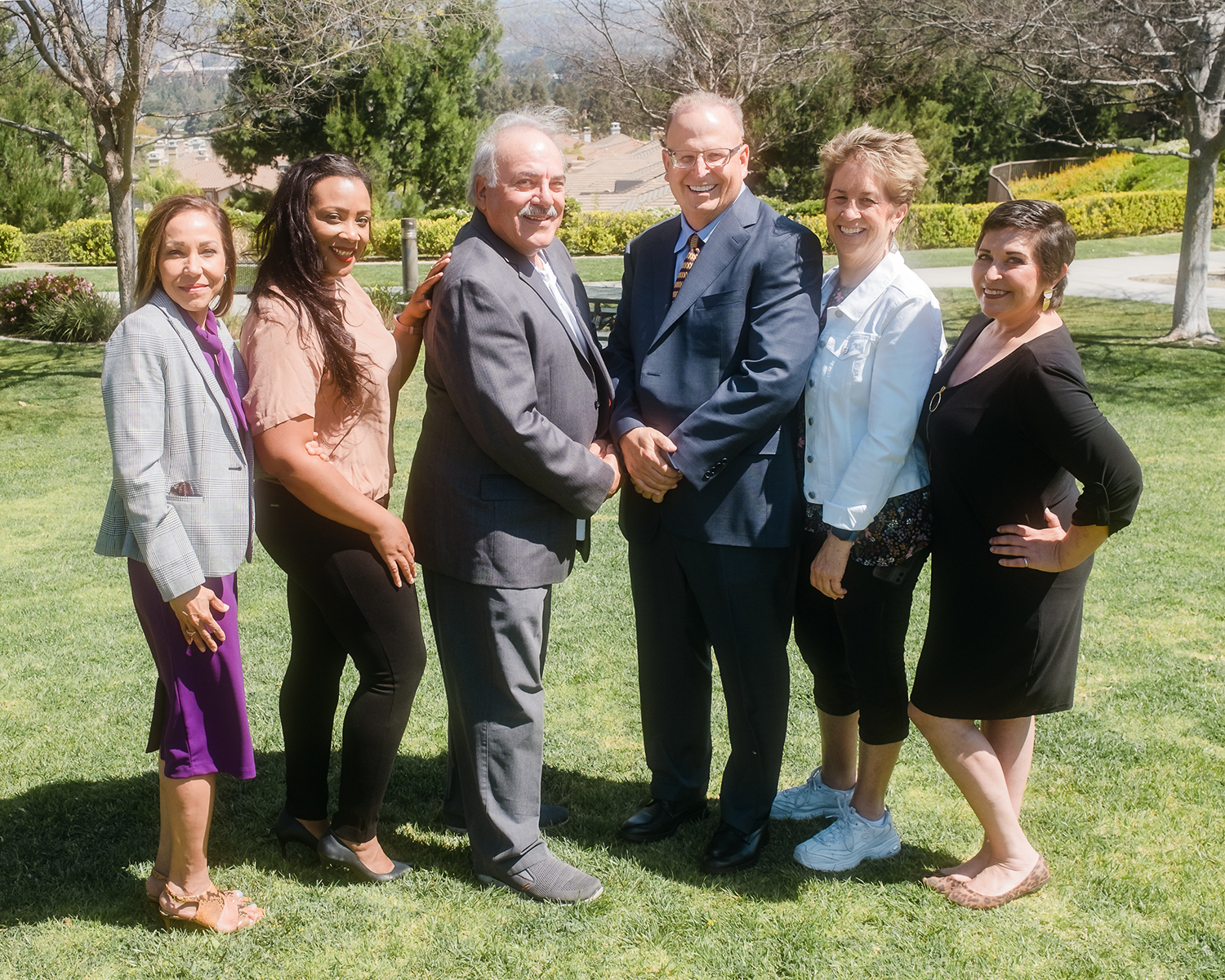 Six professional colleagues smiling outdoors on a lawn.