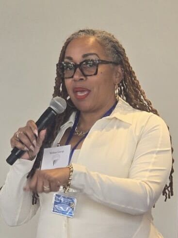 Woman with glasses and long braids speaking into a microphone