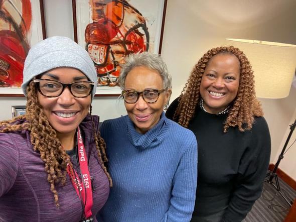 Three smiling women posing together indoors.