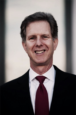 Smiling man in a black suit with a maroon tie.