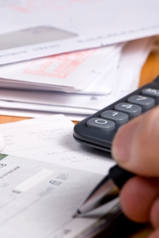Hand signing papers next to a calculator and envelopes