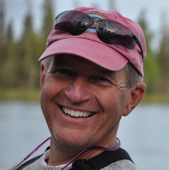 Smiling man in a pink cap and sunglasses outdoors.