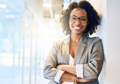 Smiling professional woman with glasses in an office corridor.