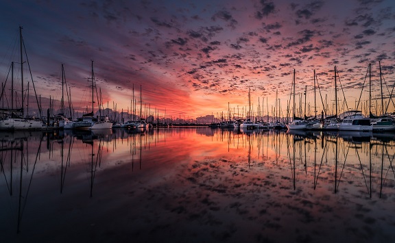Sailboats docked in a calm harbor at sunset