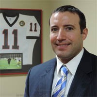 Professional man in a suit with a framed jersey behind him.