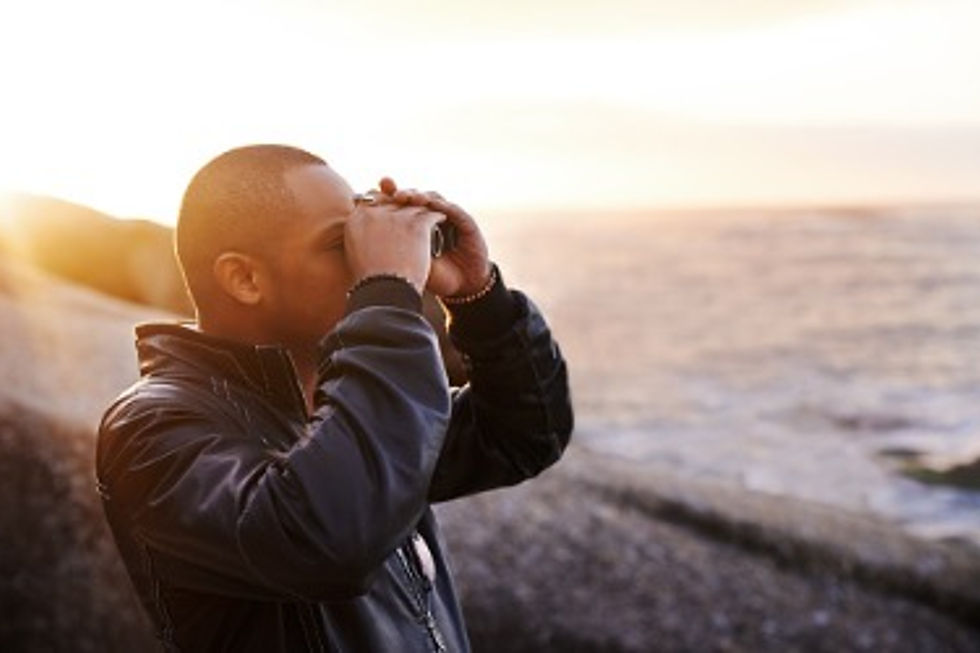 Man looking through binoculars at the sea during sunset