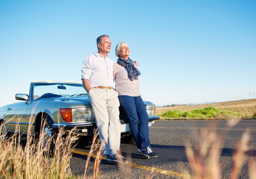 Senior couple leaning on a convertible during a road trip.