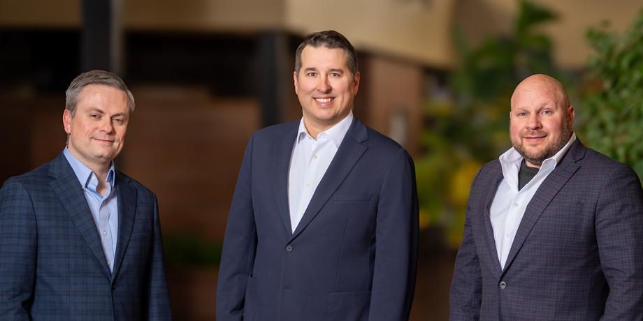 Three professional men in suits smiling in an office setting