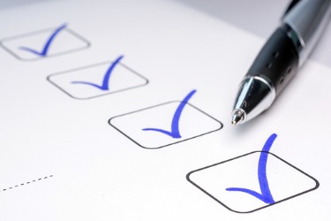 Ballpoint pen resting on a checklist with blue checkmarks