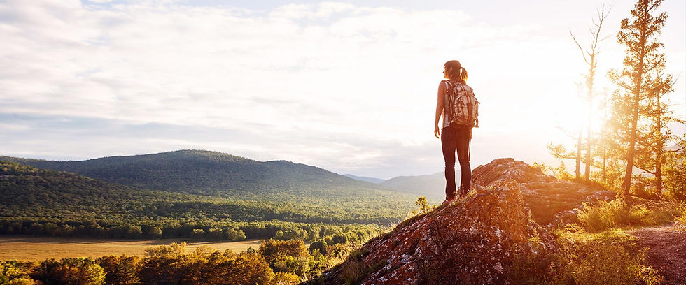 Hiker standing on a rocky peak at sunset overlooking hills