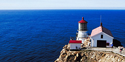 White lighthouse with red roofs on a rocky cliff by the sea