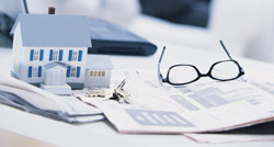 Small model house, keys, and glasses on paperwork