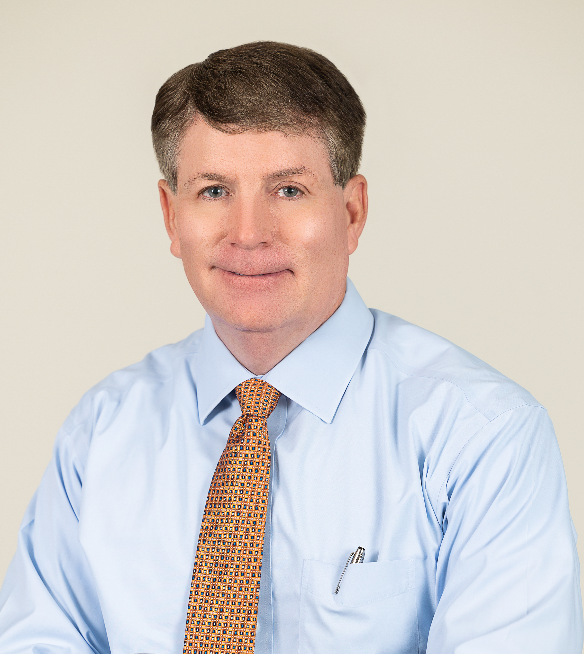 Professional headshot of a smiling man in a light blue shirt and tan tie.
