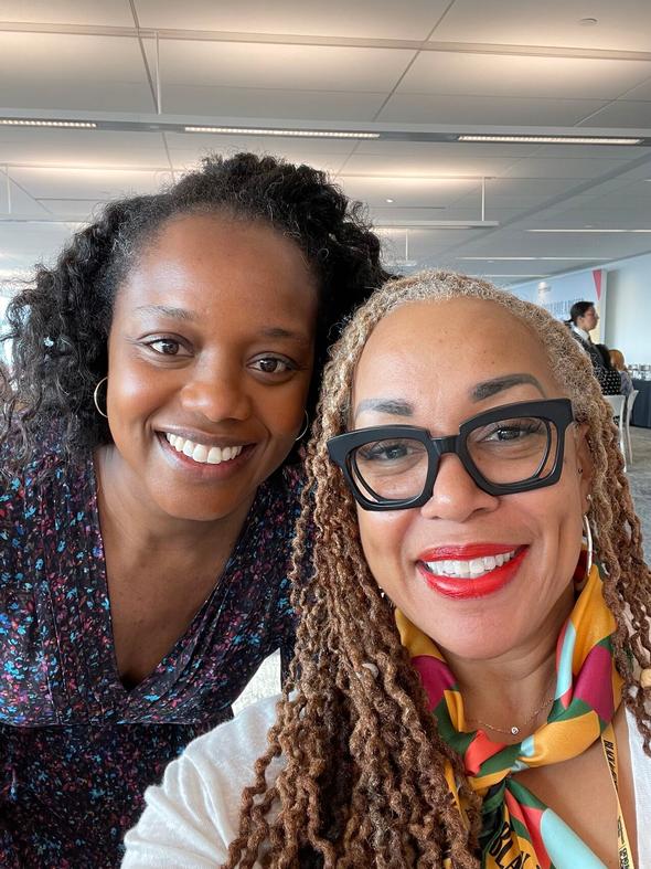 Two smiling women posing for a selfie in an office.