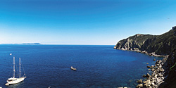 Sailboat in a calm blue bay surrounded by rocky cliffs.