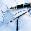 Fountain pen and eyeglasses resting on financial charts
