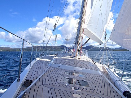 Sailboat on the water with full white sails and wood deck.