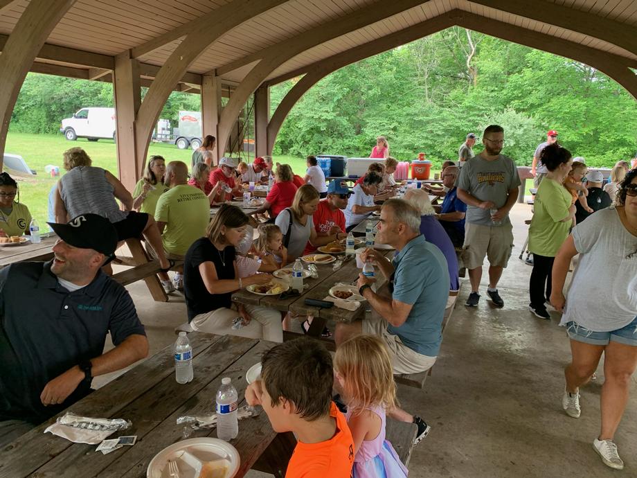 People eating at picnic tables under a pavilion pavilion.