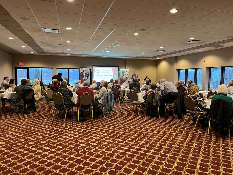 People at round tables in an event hall with a projector screen