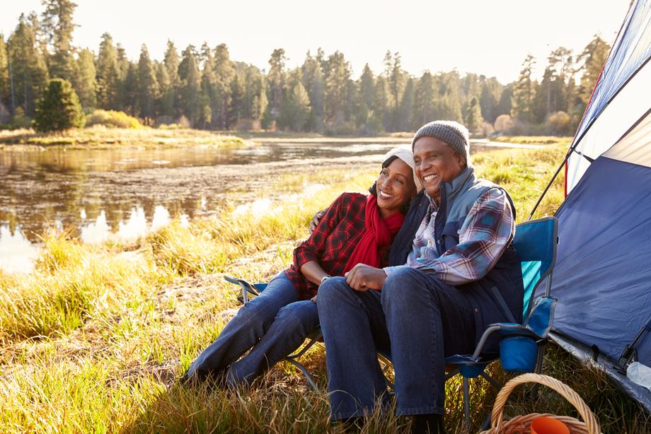 Smiling couple camping by a lake at sunset.