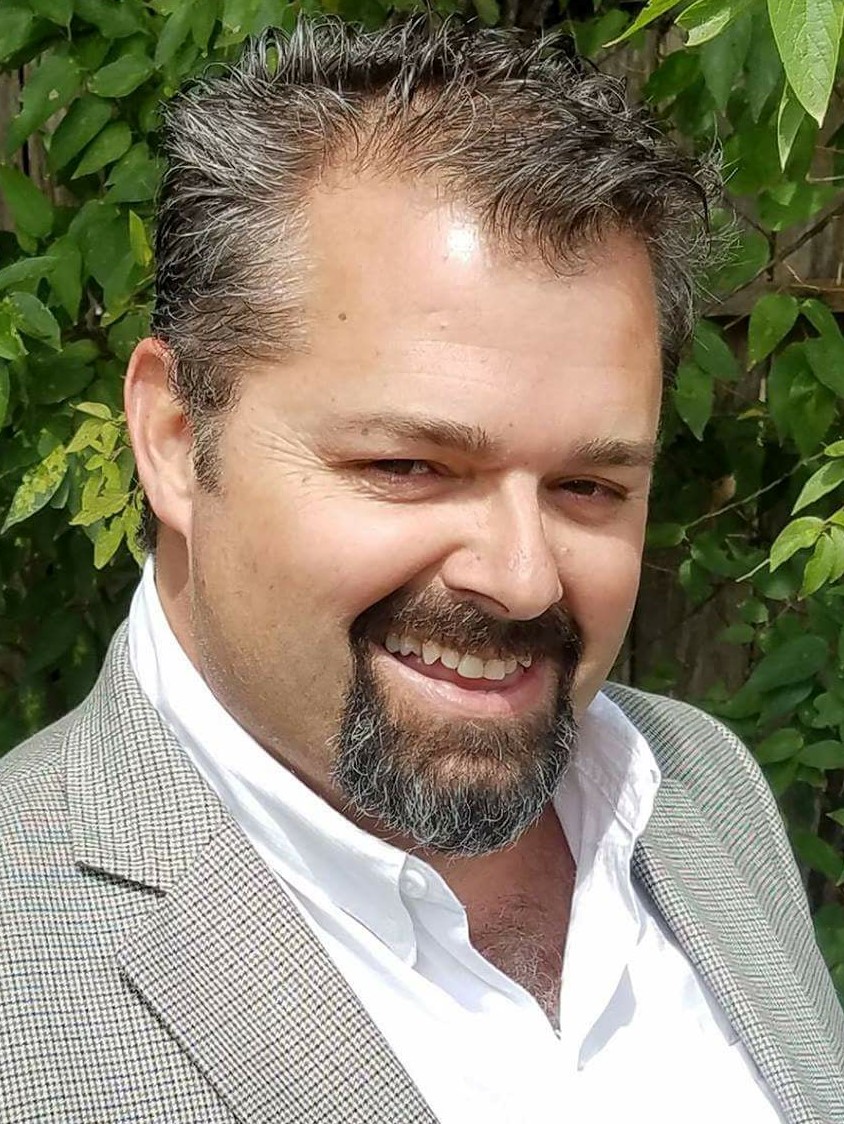 Smiling man with a goatee in a grey suit jacket