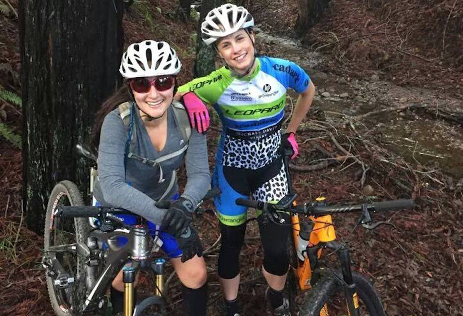 Two smiling cyclists with mountain bikes in a forest.