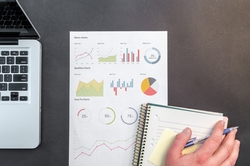 Hand writing in a notebook next to data charts and a laptop
