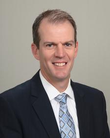 Smiling man in a suit and tie for Meet Our Team.