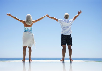 Senior couple holding hands with arms raised by the sea