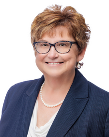 Smiling woman with glasses wearing a navy blazer and pearls