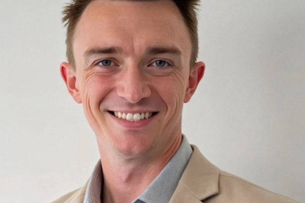 Smiling man with brown hair in a tan blazer and blue shirt