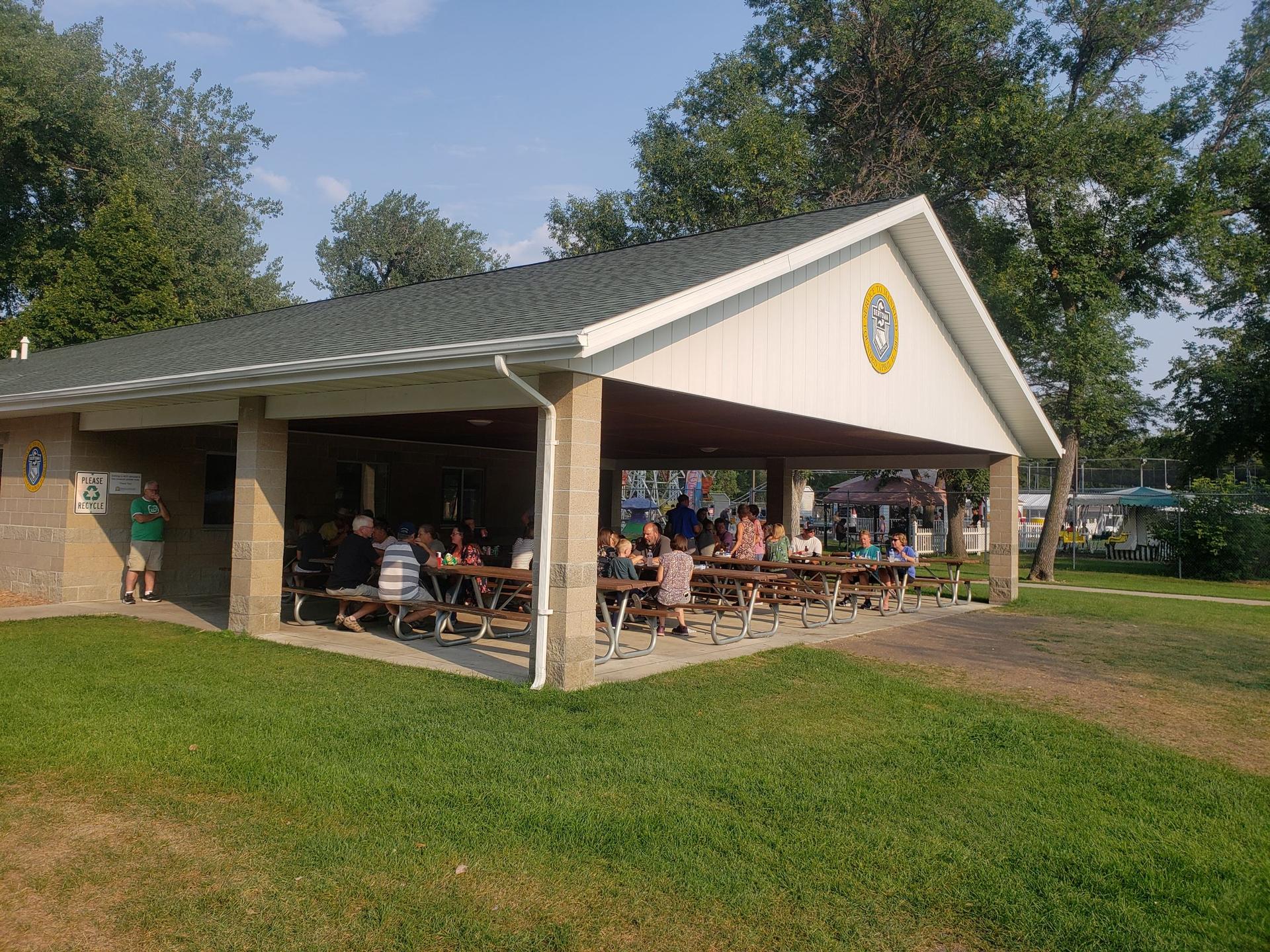 People gathering at picnic tables under a park pavilion