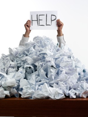 Hands holding a Help sign from under a pile of papers.