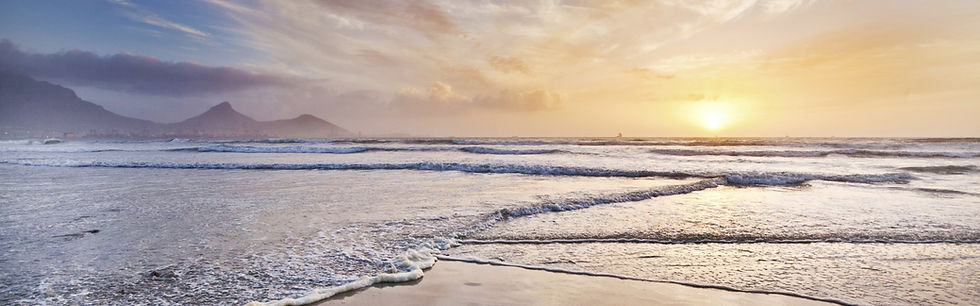 Sunset over ocean with waves on wet sand and distant mountains