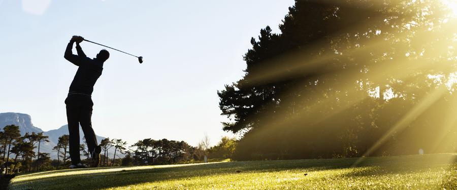 Silhouette of a golfer swinging a club at sunset.