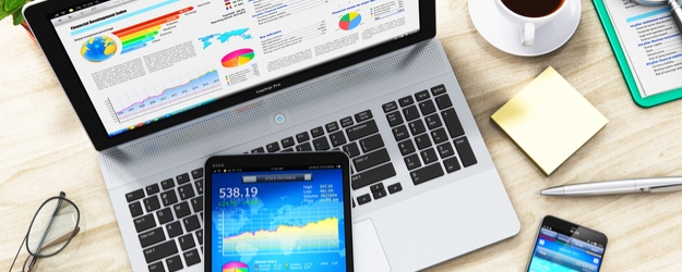 Laptop and mobile devices showing financial data and charts.