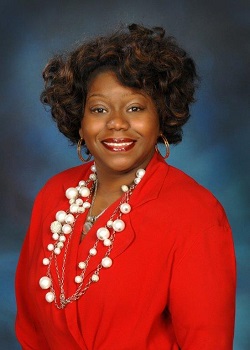 Smiling woman in a red jacket and pearl necklace.