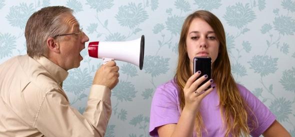 Man shouting into megaphone at girl looking at her phone.