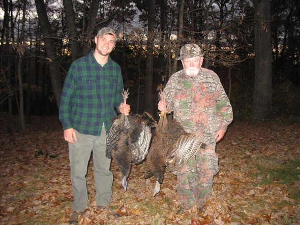 Two hunters posing with wild turkeys in the woods