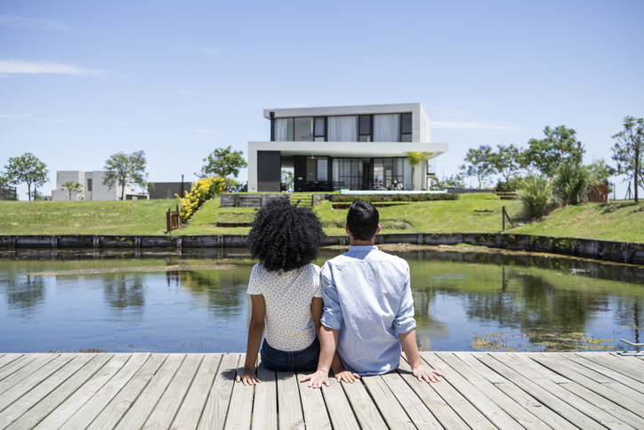 Couple sitting on a dock looking at a modern house.