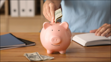 Person putting a dollar bill into a pink piggy bank.